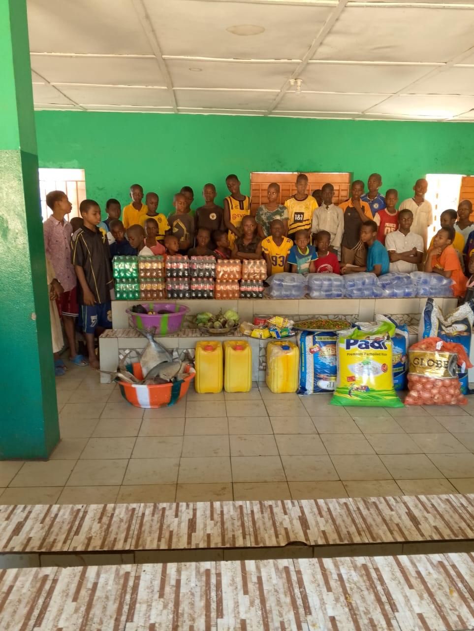 Children standing behind donated rice, oil, drinks and fresh food