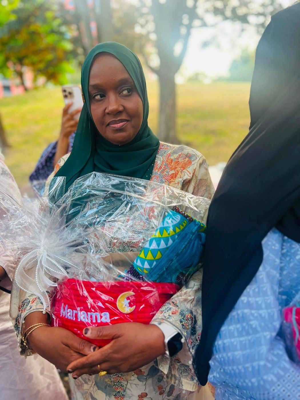 A member in a green headscarf holding a gift hamper