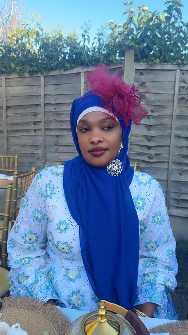 A member in a blue hijab and fascinator at a garden event