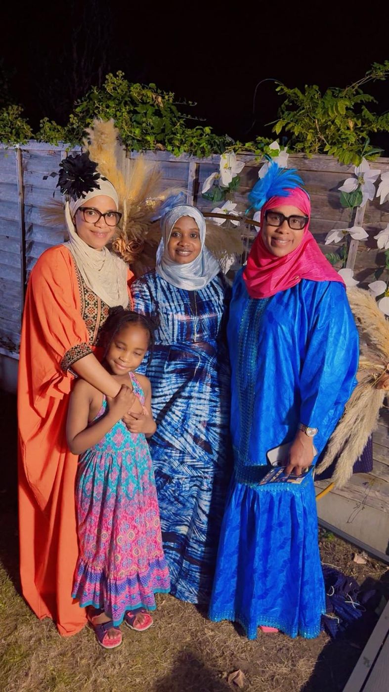 Two members in orange and blue gowns with a young girl at a garden event
