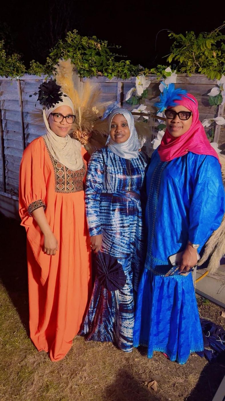 Three members in orange and blue traditional gowns in a garden