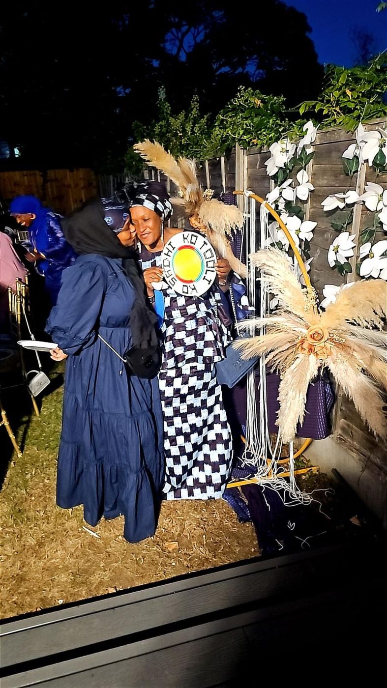 Two members in indigo and patterned gowns at a garden event
