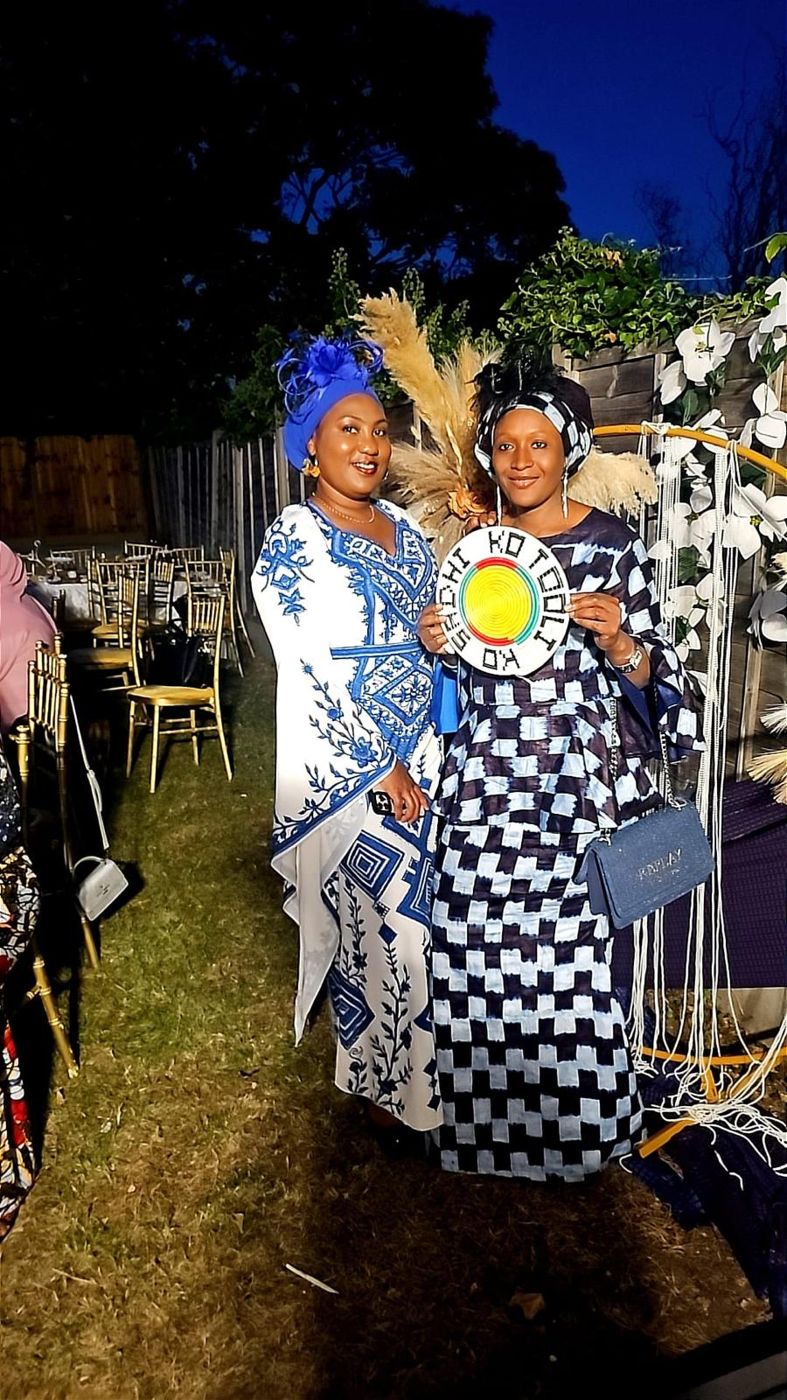 Two members in black and white patterned gowns holding a decorative sign