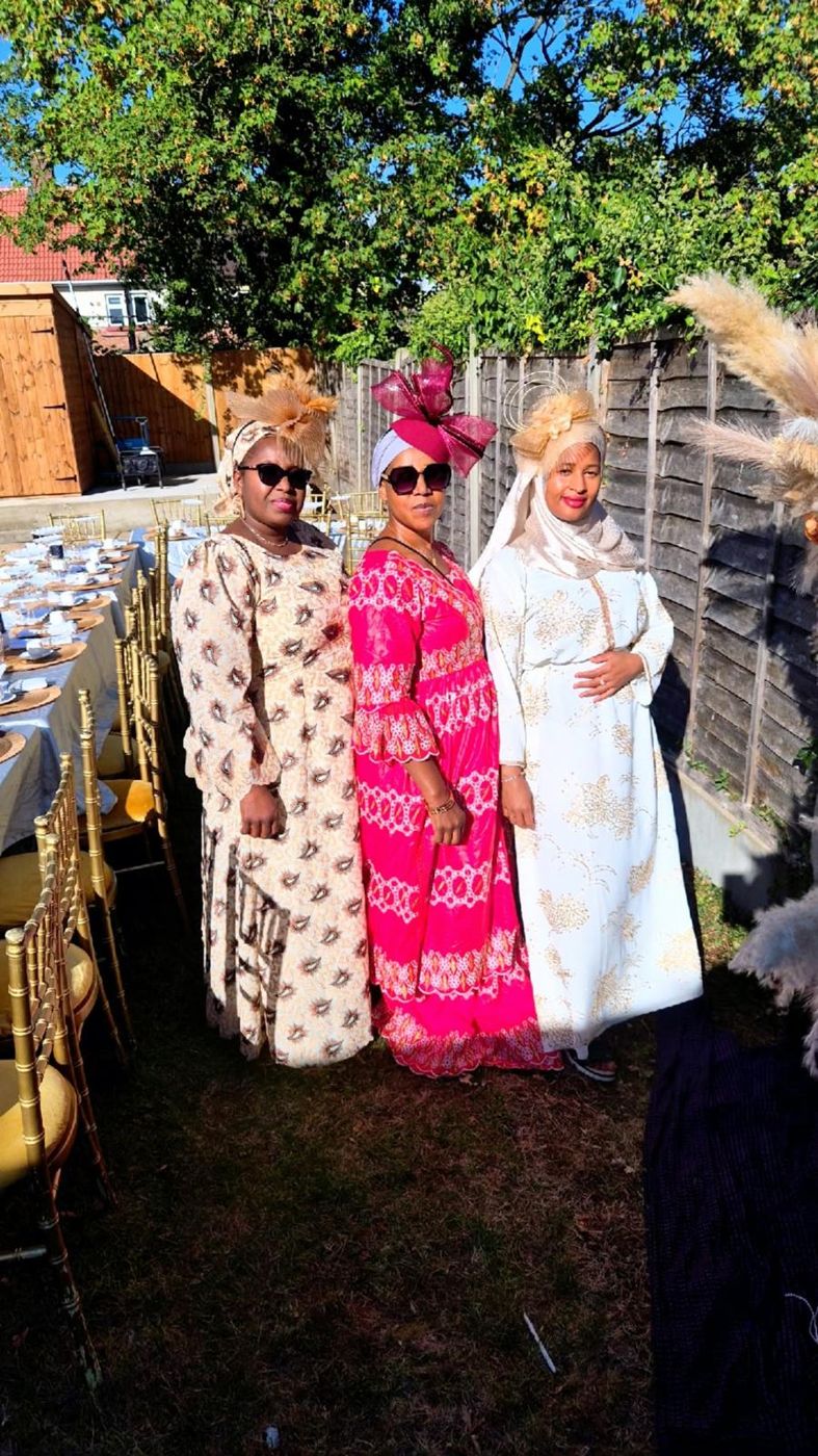 Three members in traditional outfits and headwraps at a garden event
