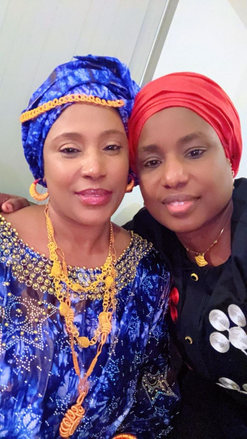 Two members smiling in colourful headwraps and jewellery