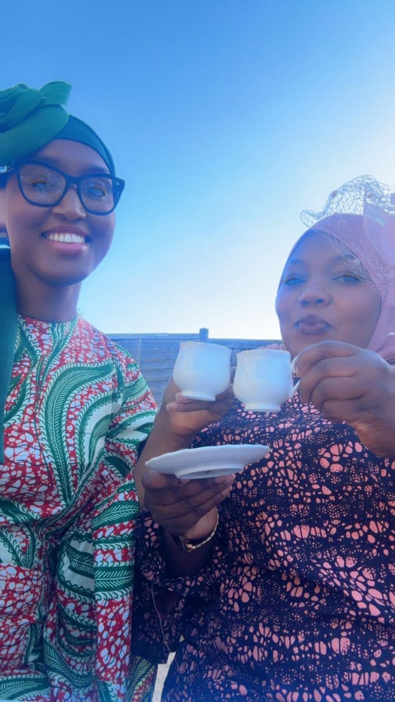 Two friends smiling and holding teacups under a blue sky